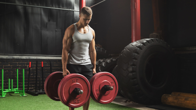 A muscular person doing farmer's carry exercise in the gym.