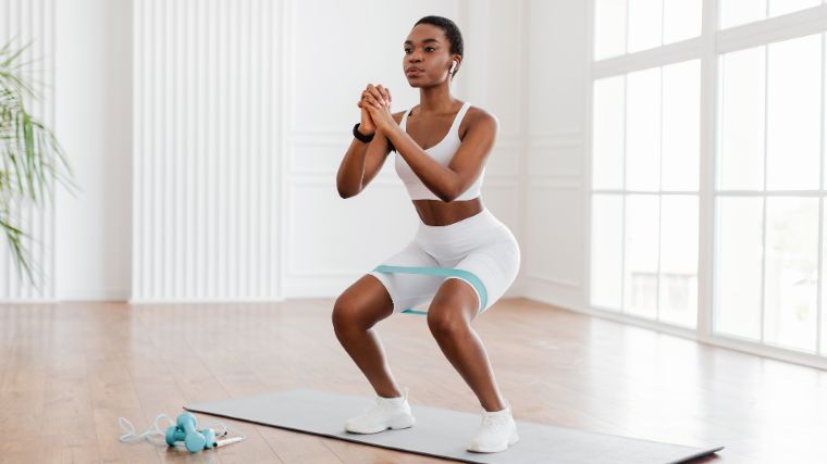 A person doing air squats with resistance band at home.