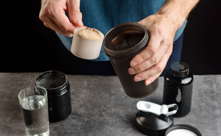 A person scooping out protein powder into a container.