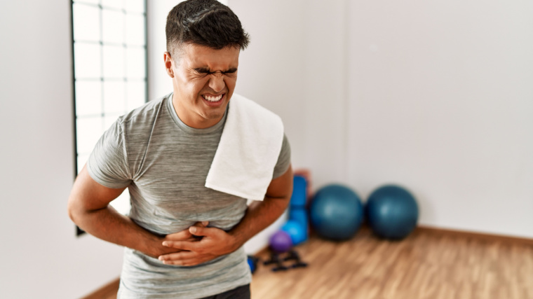 A person wearing sportswear and towel at the gym with hands on their stomach because of pain. 