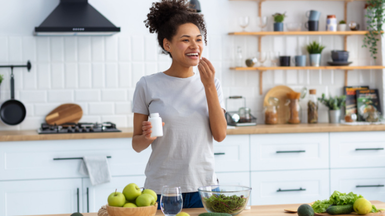 A person taking a probiotic supplement in their kitchen. 