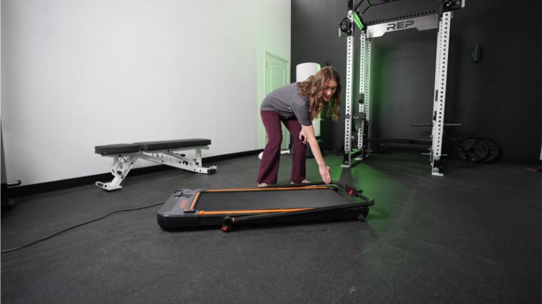 A woman is shown folding the handlebar on the UREVO 2-in-1 Under Desk Treadmill.
