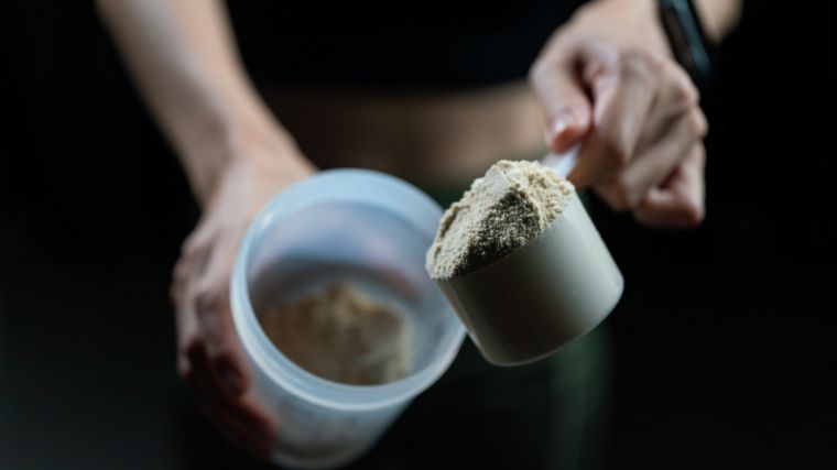 Whey protein powder being scooped into a shaker bottle.