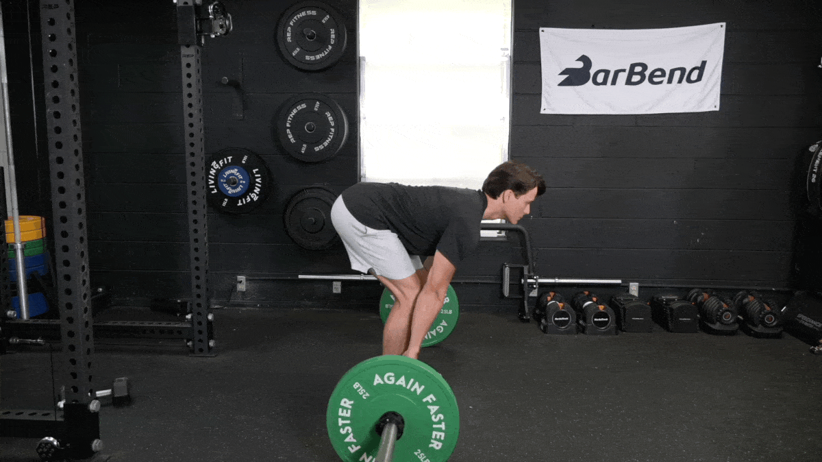 Person in silver shorts and black t-shirt performing a Romanian deadlift with a loaded barbell.