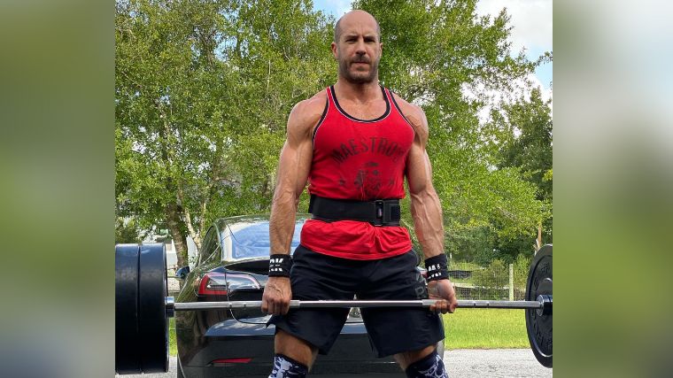 Claudio Castagnoli deadlifts outside in front of a car.