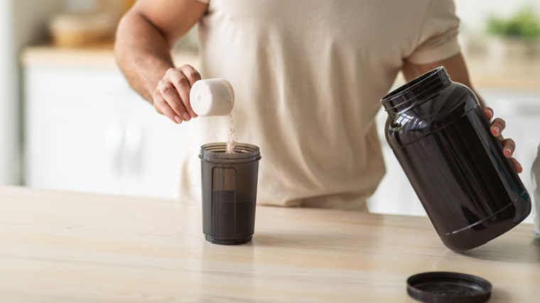 A person pouring a scoop filled with powdered supplements into the shaker.